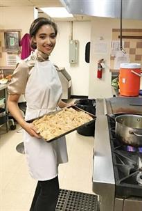 Woman in apron holds a tray of baked goods